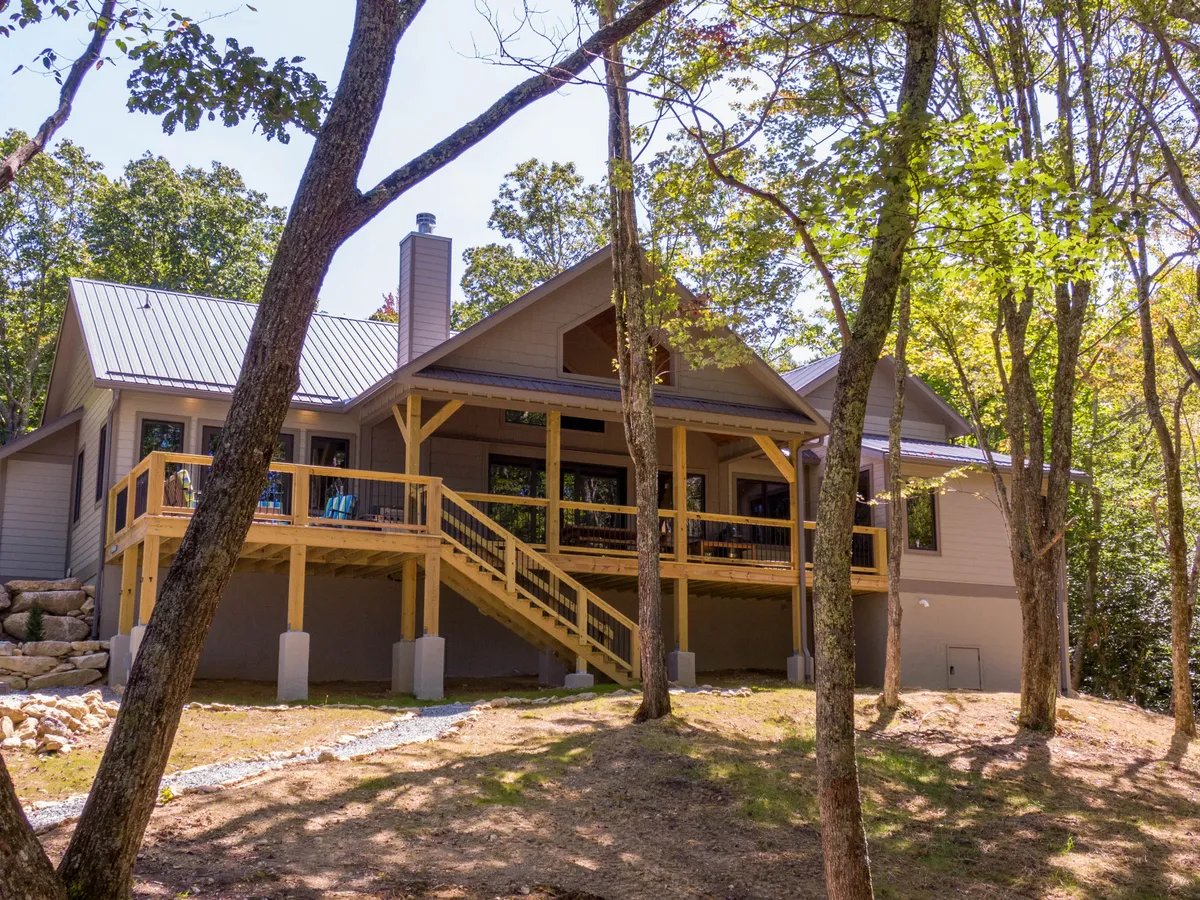 A welcoming home exterior with a front porch, staircase, large windows, chimney, and surrounding trees. The porch invites outdoor relaxation, family gatherings, and enjoying the sights and sounds of nature right at your doorstep.