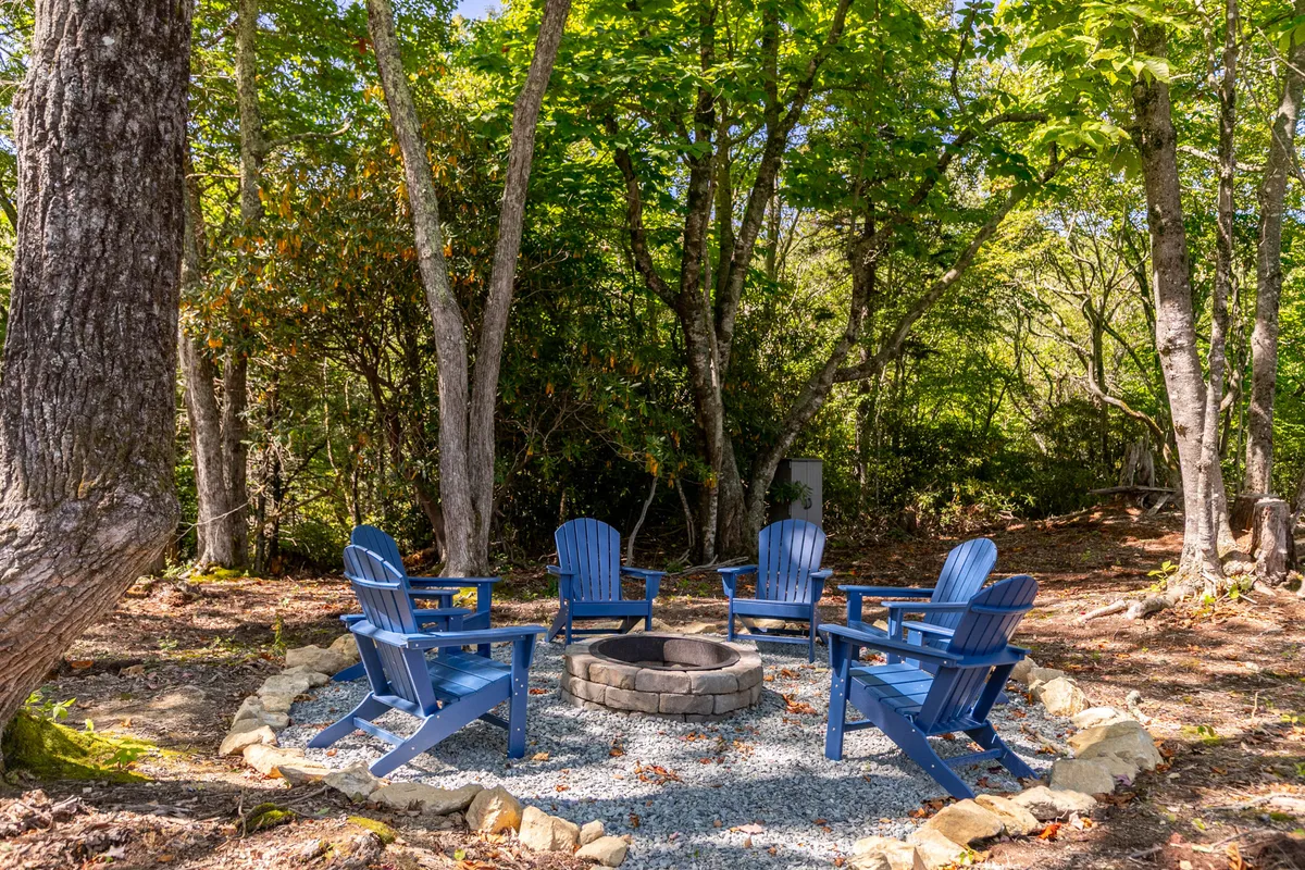 A cozy outdoor fire pit surrounded by blue chairs, nestled among trees. The arrangement invites groups to gather, share stories, and enjoy the warmth of a campfire under the stars.