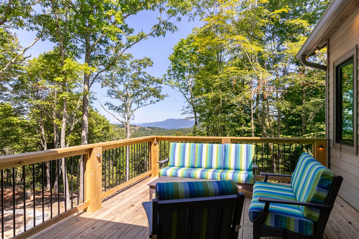 A wooden deck furnished with striped outdoor sofas overlooks lush greenery and distant mountain views. The setting is ideal for relaxing, reading, or enjoying a cup of coffee while immersed in nature, with the deck blending indoor comfort and outdoor beauty.