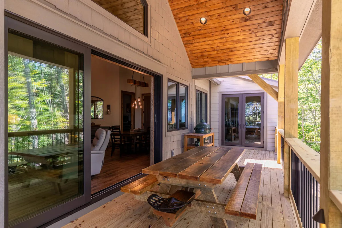 A welcoming outdoor scene with a wooden picnic table adjacent to large windows and an outdoor seating area, inviting guests to enjoy alfresco dining and gatherings while surrounded by natural beauty.