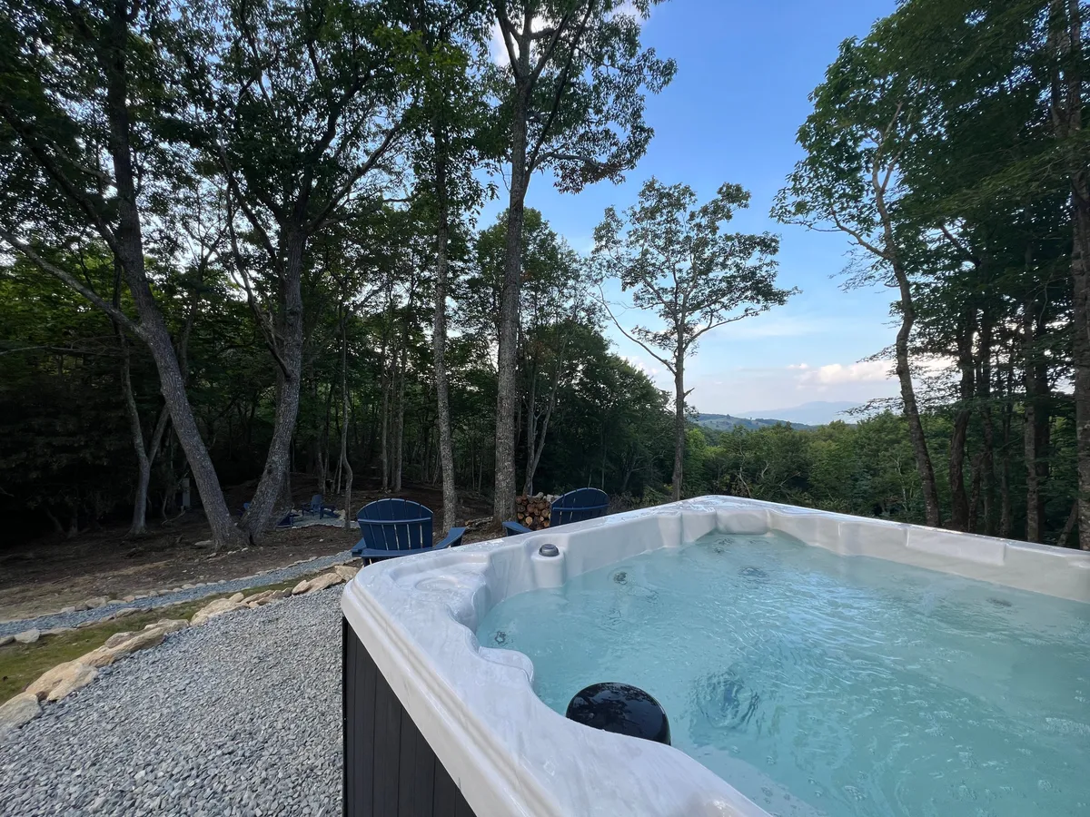 A tranquil outdoor hot tub area nestled among trees, with comfortable seating nearby. The scene exudes privacy and peace, perfect for an early morning soak or nighttime stargazing.