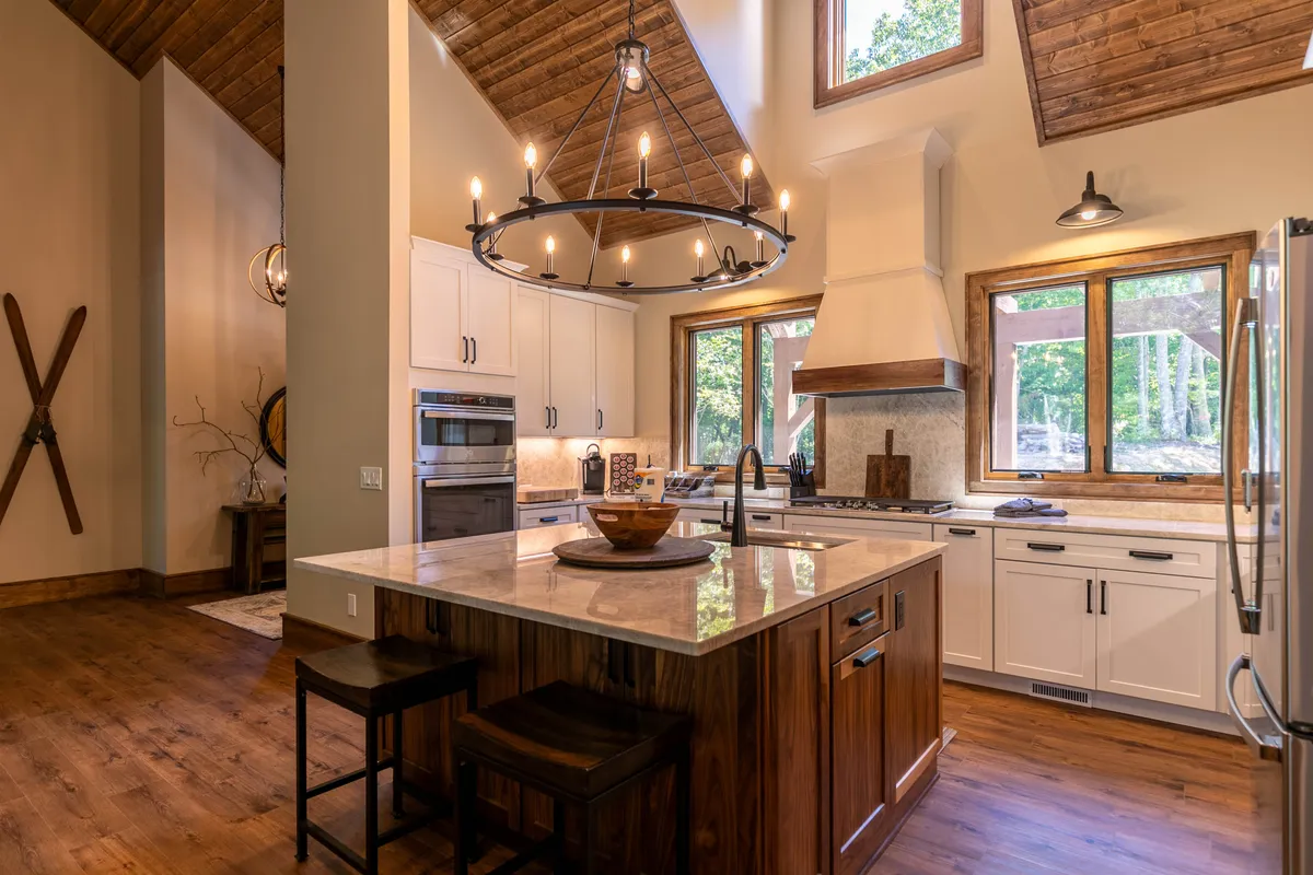 An inviting kitchen with a central granite island, elegant chandelier lighting, expansive windows, and rich wooden cabinetry. The setup highlights ample space for cooking, socializing, and enjoying meals together.
