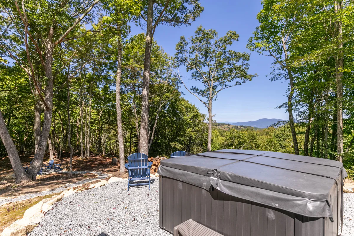 The image shows a hot tub and blue chairs set among trees, with a breathtaking mountain view in the background. This tranquil corner offers a serene spot for soaking, stargazing, or sipping morning coffee, highlighting luxurious outdoor amenities.